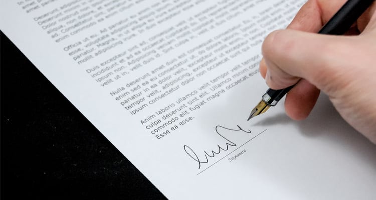 Uma folha de papel com o texto de contrato sendo assinada por uma caneta tinteiro