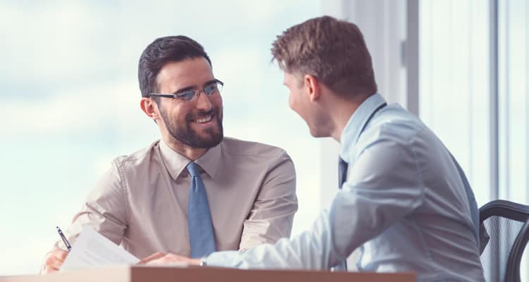 Homens sentados ao redor de uma mesa, usando roupas sociais e conversando